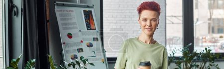 smiling queer person with takeaway drink in paper cup looking at camera in modern office, banner