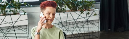 positive queer person with short hair talking on mobile phone in modern office, horizontal banner
