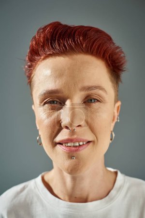 Photo for Close up portrait of redhead bigender person with facial piercing looking at camera on grey backdrop - Royalty Free Image