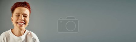 Foto de Retrato de pelirroja persona más grande con piercing facial riendo con los ojos cerrados en gris, bandera - Imagen libre de derechos