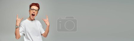 Foto de Persona grande emocionado en gafas que muestran el signo de roca con las manos y gritando en gris, pancarta - Imagen libre de derechos