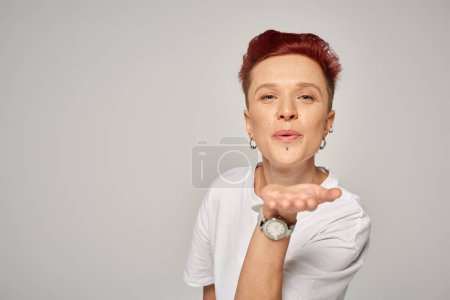 Photo for Redhead queer person in white t-shirt blowing air kiss and looking at camera on grey backdrop - Royalty Free Image