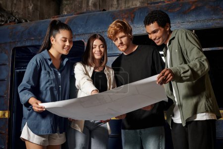 Gruppe fröhlicher junger multikultureller Freunde löst Quest-Aufgabe, während sie im Escape Room auf die Landkarte schaut
