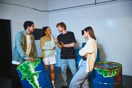 Foto de Grupo joven interracial de amigos charlando cerca de barriles oxidados y resolver la búsqueda en la sala de escape - Imagen libre de derechos