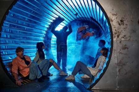 amigos multiétnicos sentados en un túnel cerca de gente rara con máscaras de gas, aventura en la sala de misiones
