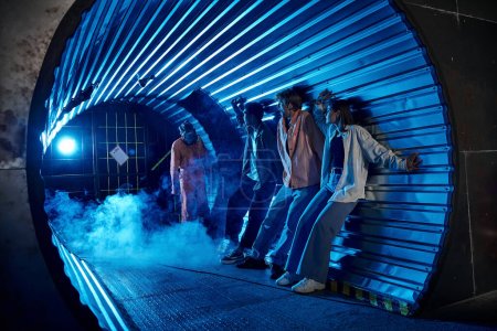 amis multiethniques debout dans le tunnel près de gens bizarres en masques à gaz, aventure de la salle de quête