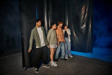 grupo de cuatro amigos interracial asustados de pie dentro de la sala de escape durante la búsqueda