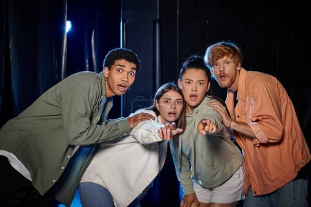 group of diverse astonished friends discovering a clue in escape room, women pointing with finger