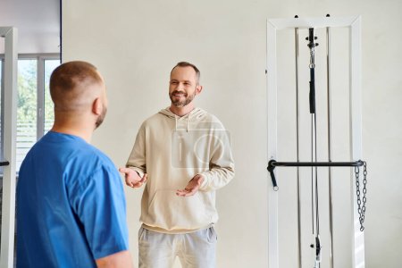 hombre positivo hablando con el médico en uniforme azul durante la cita en el centro kinesio rehabilitación