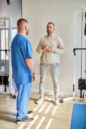 schöner Mann diskutiert Behandlungsplan mit Arzt in blauer Uniform im Rehabilitationszentrum