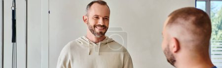 handsome bearded man smiling near young recovery specialist in kinesio center, horizontal banner