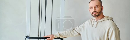 patient masculin barbu debout près de la machine d'exercice dans la salle de gym du centre de kinésiologie moderne, bannière