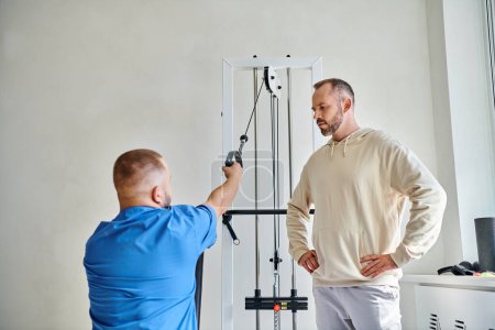 young recovery expert working out on exercise machine, instruction of man in kinesio center
