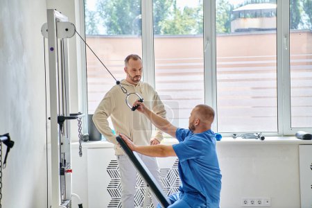professional rehabilitologist training on exercise machine, instruction of man in kinesio center