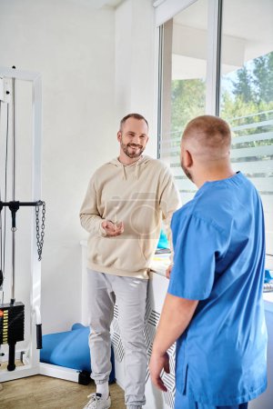 smiling man talking to young  doctor in blue uniform during appointment in kinesio center