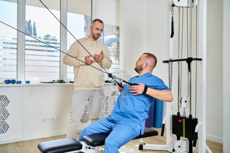 skilled rehabilitation specialist showing exercise on training machine to man in kinesiology center
