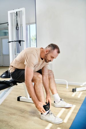 hombre en ropa deportiva poniendo cinturón de pierna fitness antes del entrenamiento de recuperación en el moderno centro de kinesiología