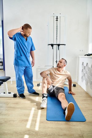 Téléchargez les photos : Réhabilitologue parler à l'homme assis sur le fitness homme près de la machine d'entraînement dans le centre de kinesio - en image libre de droit