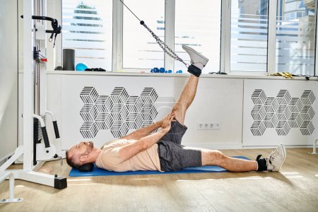 man in sportswear lying on fitness mat and working out on exercise machine in gym of kinesio center
