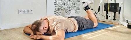 man lying face down on fitness mat and training on exercise machine in kinesio center, banner
