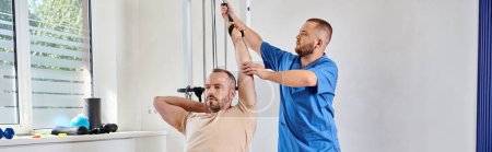 Photo for Doctor in blue uniform assisting man working out on exercise machine in kinesio center, banner - Royalty Free Image