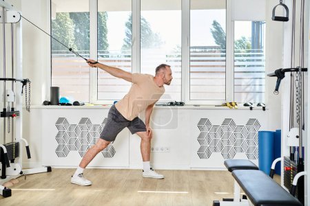 Photo for Athletic man in sportswear working out on exercise machine in gym of modern kinesio center, recovery - Royalty Free Image