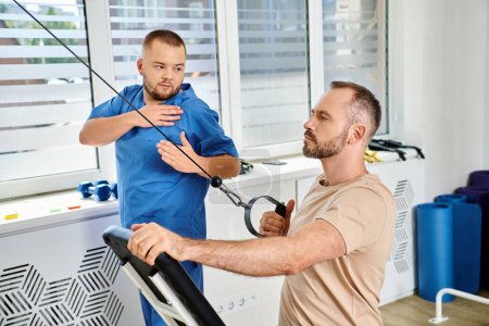 young rehabilitologist in blue uniform assisting man during recovery training in kinesio center