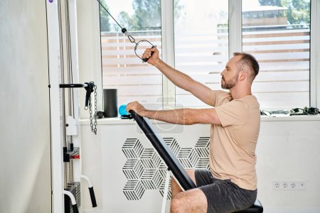 Photo for Side view of handsome man in sportswear working out on training machine in kinesiology center - Royalty Free Image