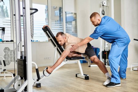 Foto de Médico en uniforme azul ayudando al hombre durante el entrenamiento de recuperación en la máquina de ejercicio en el centro kinesio - Imagen libre de derechos