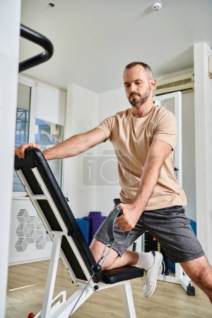 Photo for Handsome man in sportswear training on exercise machine in modern gym of kinesio center, recovery - Royalty Free Image