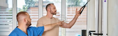Téléchargez les photos : Docteur qualifié en uniforme bleu instruisant l'homme dans la salle de gym du centre kinesio, bannière horizontale - en image libre de droit