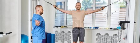 Photo for Recovery specialist assisting man training on exercise machine in modern kinesio center, banner - Royalty Free Image