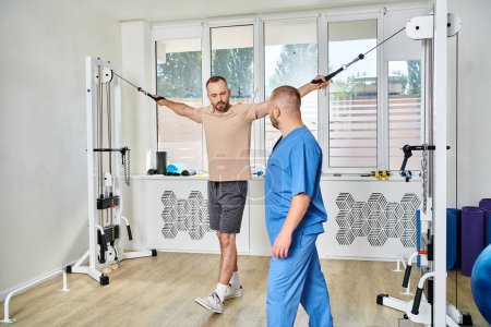 Photo for Young physiotherapist assisting male patient working out on exercise machine in kinesio center - Royalty Free Image