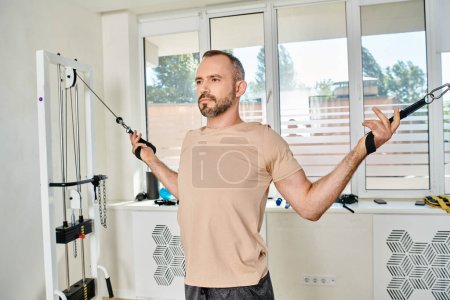 sportive handsome man training arms on modern exercise machine in kinesio center, recovery fitness
