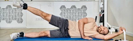 bearded man lying down on fitness mat and training on exercise machine in kinesio center, banner