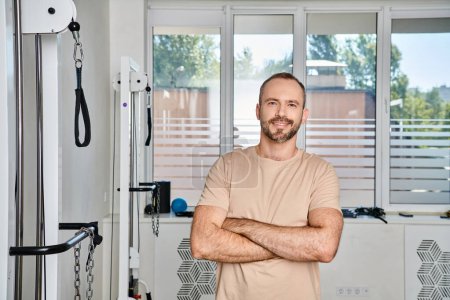 Photo for Happy and handsome man with folded arms looking at camera in gym of modern kinesiology center - Royalty Free Image