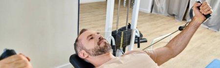 Photo for Handsome man in sportswear training arms on exercise machine in kinesio center, banner - Royalty Free Image