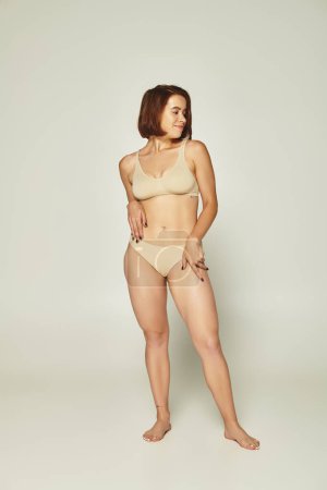 body positive concept, full length of woman in underwear smiling and posing on grey background