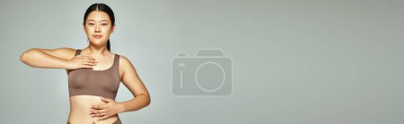 banner of young asian woman with brunette hair posing in brown lingerie on neutral grey background