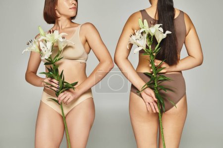 Photo for Cropped woman in beige lingerie standing near female friend and holding flowers in hands on grey - Royalty Free Image