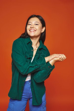 strahlende junge Asiatin posiert in lebendigem Outfit und blickt in die Kamera auf orangefarbenem Hintergrund