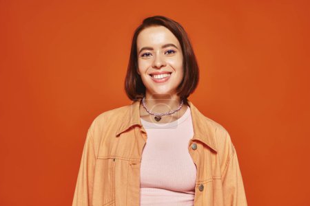 Photo for Cheerful young woman with short hair looking at camera and smiling on orange background, carefree - Royalty Free Image