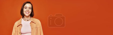 Foto de Alegre joven con el pelo corto mirando a la cámara y sonriendo sobre fondo naranja, pancarta - Imagen libre de derechos