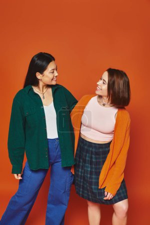 zwei Frauen in lässiger Kleidung, die sich umarmen und glückliche Momente miteinander auf orangefarbenem Hintergrund teilen