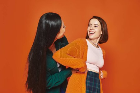 freudige Freunde in lässiger Kleidung umarmen sich und teilen glückliche Momente gemeinsam auf orangefarbenem Hintergrund