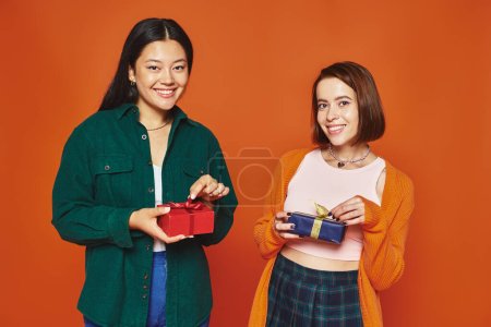 multiethnic friends exchanging gifts, smiling and having great time on orange background, joy