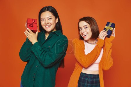 happy multicultural friends exchanging gifts, smiling and having a good time on orange backdrop