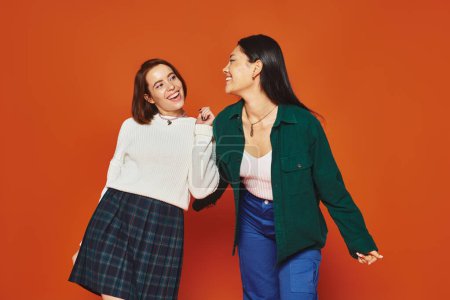 Photo for Happy multicultural female friends in vibrant attire looking at each other on orange background - Royalty Free Image
