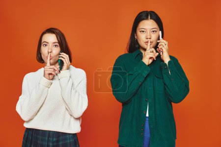 Diverse Frauen in lebendiger Kleidung unterhalten sich auf Mobiltelefonen und zeigen Schweigezeichen auf orangefarbenem Hintergrund