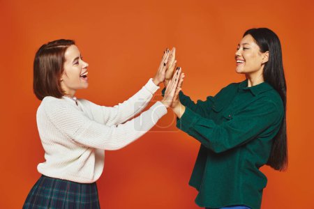 glückliche junge multikulturelle Freunde in lebendiger Kleidung geben High Five auf orangefarbenem Hintergrund